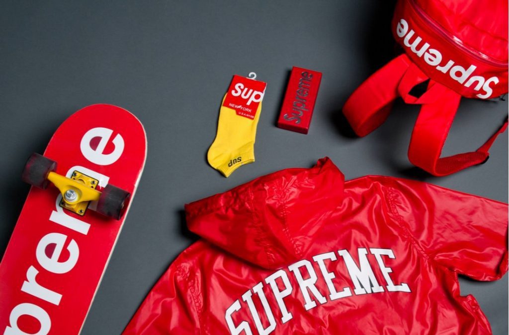 Red and white Supreme backpack, skateboard, and shirt on black background
