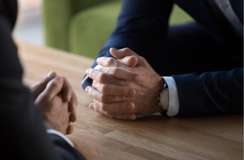 Clasped male hands of two businessmen negotiate at table