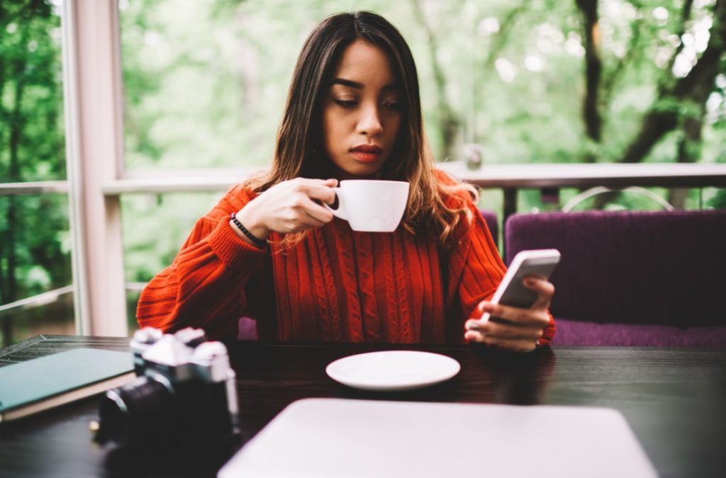 Woman drinking coffee looking upset at smartphone